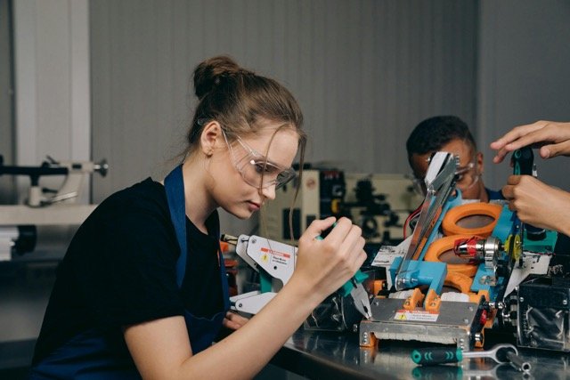 A woman in a black shirt holding pliers in Apprenticeship